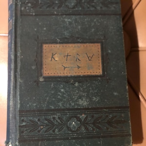 May include: A dark green hardcover book with gold lettering on the spine and front cover. The front cover has a decorative border and the text "K.T.R.W." in a gold rectangle.