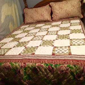 May include: A bed with a wooden headboard, two decorative pillows, and a patchwork quilt. The quilt features a pattern of white and green squares with floral accents. The bed skirt has a floral design with pink and green flowers.