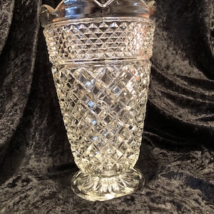 May include: Clear glass vase with a diamond pattern and scalloped rim. The vase has a wide, flared shape and a decorative base. The glass is thick and has a high level of clarity, reflecting light.