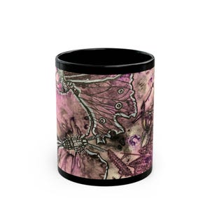 May include: A cylindrical ceramic mug with a black interior and rim. The exterior features a detailed watercolor-style illustration of moths and botanical elements in shades of muted pink, deep purple, and dark brown ink outlines.