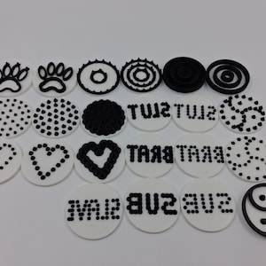 May include: A collection of white, circular decorations with black designs. The designs include paw prints, dots, hearts, and text. One decoration features a yin-yang symbol. The decorations are arranged on a white surface.