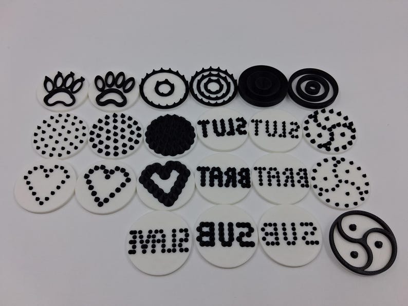 May include: A collection of white, circular decorations with black designs. The designs include paw prints, dots, hearts, and text. One decoration features a yin-yang symbol. The decorations are arranged on a white surface.