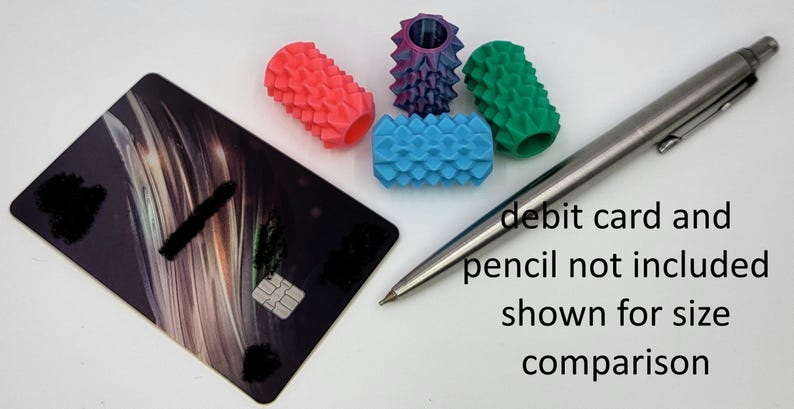 May include: Four cylindrical pencil grips with textured, spiked surfaces in coral, purple, green, and blue. A black debit card and a silver mechanical pencil are positioned nearby for size comparison, with text stating debit card and pencil not included.