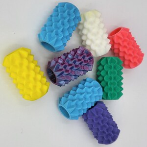 May include: A collection of eight cylindrical, hollow, textured sensory rollers in various colors including blue, white, coral, yellow, purple, green, and light blue. Each roller features a repeating geometric, spiked surface pattern.