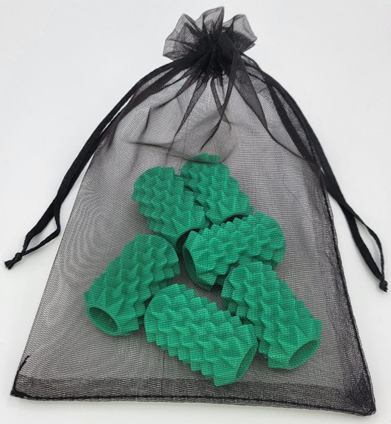 May include: A black sheer drawstring mesh bag containing five cylindrical green pencil grips. Each grip features a textured, spiked surface pattern and a hollow center, designed to slide onto a standard writing instrument for added grip.