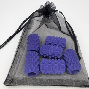 May include: A set of five purple cylindrical objects with a textured, spiked surface, contained within a sheer black drawstring mesh bag. Each purple piece features a hollow center and a repeating geometric pattern of pointed protrusions.