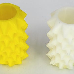 May include: Two cylindrical objects with a textured, spiked exterior surface. One object is bright yellow and the other is off-white. Both items feature a hollow center and a repeating geometric pattern of pointed protrusions along their vertical sides.