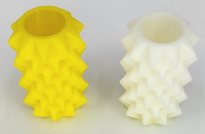 May include: Two cylindrical objects with a textured, spiked exterior surface. One object is bright yellow and the other is off-white. Both items feature a hollow center and a repeating geometric pattern of pointed protrusions along their vertical sides.