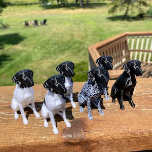 May include: Five small dog figurines in a sitting position, each featuring a black head and ears. The bodies vary in color and pattern, including solid white, white with black spots, a blue and black speckled finish, and a solid black design.