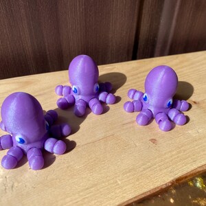 May include: Three purple octopus figurines with blue eyes. The octopus figurines are made of a shiny plastic material.
