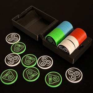 Puede incluir: Un conjunto de fichas y tokens de juego coloridos. Las fichas están apiladas en una caja negra y son azules, verdes, blancas y rojas. Los tokens son negros con diseños blancos y verdes. Las piezas del juego están sobre una superficie negra.