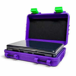 May include: A rectangular purple protective storage case with bright green latches and hinges. The case is open, revealing a black foam interior lining and a dark, rectangular electronic device with a glossy screen resting inside the base.