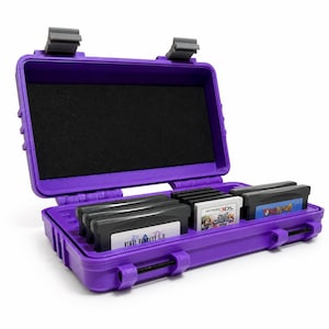 May include: A purple hard-shell storage case with two gray latches, featuring a black foam-lined interior. The case holds several rectangular video game cartridges, including titles labeled Final Fantasy I & II, Super Smash Bros, and Yoshi Island.