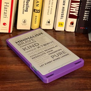 May include: A rectangular e-reader device with a purple frame and a light gray screen displaying the text: UNCOMPROMISING MINIMALISM, BRAVE, CONFIDENCE, KIND, UNIQUE XTEINK, INDEPENDENT, EXCELLENCE READING AT FINGERTIPS, RESOLUTE, PURE, LET EVERY WORD LINGER.