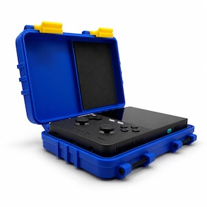 May include: A black handheld video game console with dual analog sticks and buttons, resting inside a bright blue protective hard-shell carrying case. The case features two yellow latches at the top and a black foam insert on the interior lid.