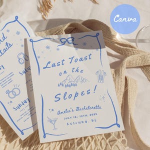 May include: A blue and white invitation card with a blue border and a snowflake design. The text on the card reads "Last Toast on the Slopes!" and "Amelia's Bachelorette July 12-14th, 2025 Kelowna, BC".