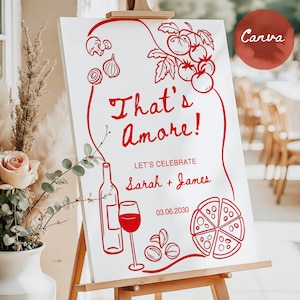 May include: White sign on a wooden easel with red line art. The sign says "That's Amore!" and includes illustrations of tomatoes, onions, a wine bottle, a glass of wine, olives, and a pizza. The sign also says "Let's Celebrate Sarah + James" and the date.