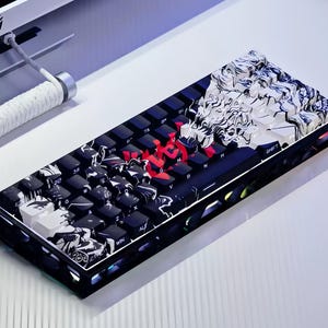 May include: A custom mechanical keyboard in black and white. The keys are black with white lettering, and some have a red accent. The keyboard features a distinctive artistic design on the top. The keyboard is connected by a white cable.