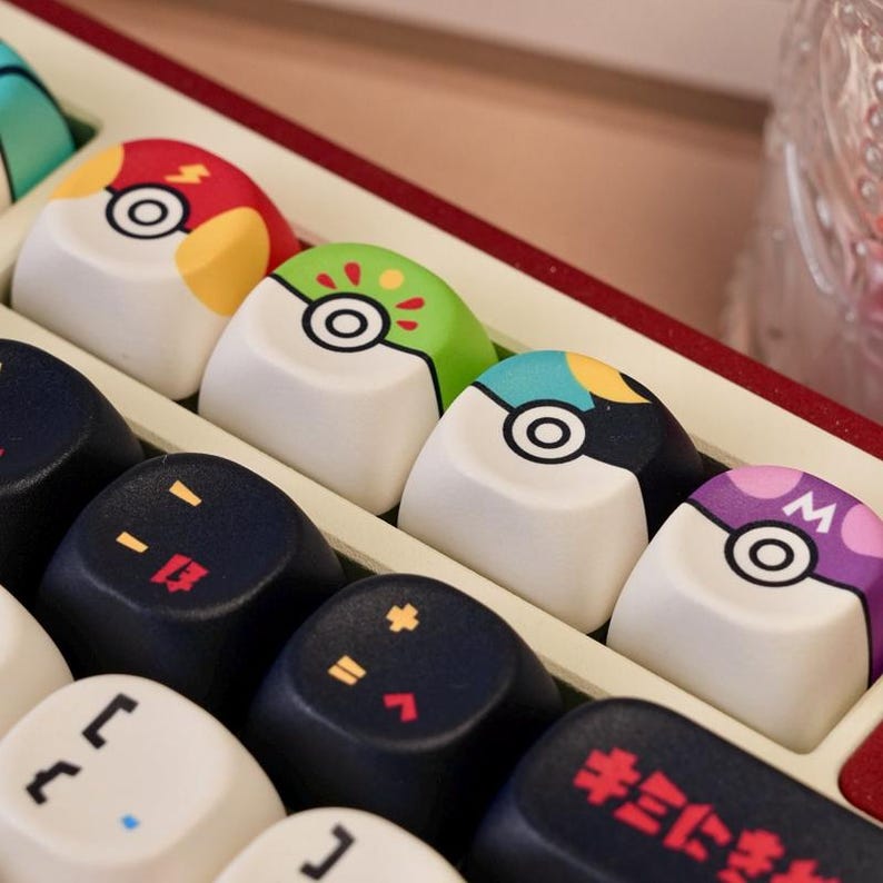 May include: Close-up of a keyboard with custom keycaps. The keycaps feature colorful designs, including red, yellow, green, blue, and purple, with circular patterns and the letter "M". The keyboard keys are arranged in rows within a red-trimmed frame.