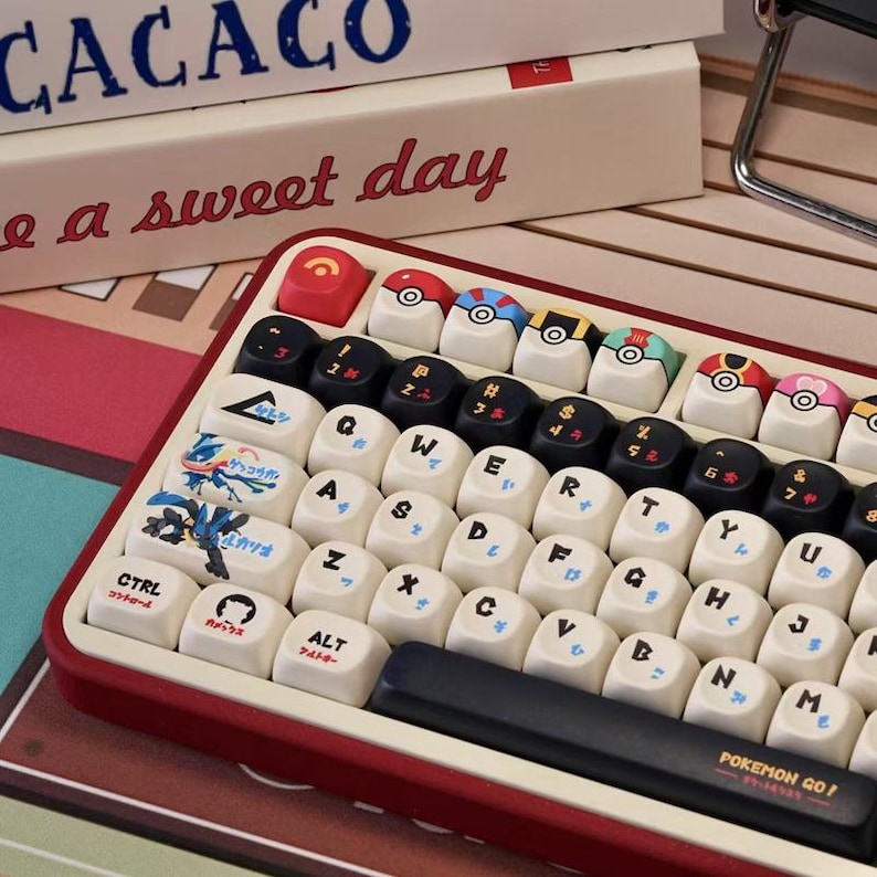 May include: A red and white keyboard with custom keycaps. The keycaps feature various designs, including Pokeball graphics and Japanese text. The keyboard also has the text "POKEMON GO!" on the spacebar.