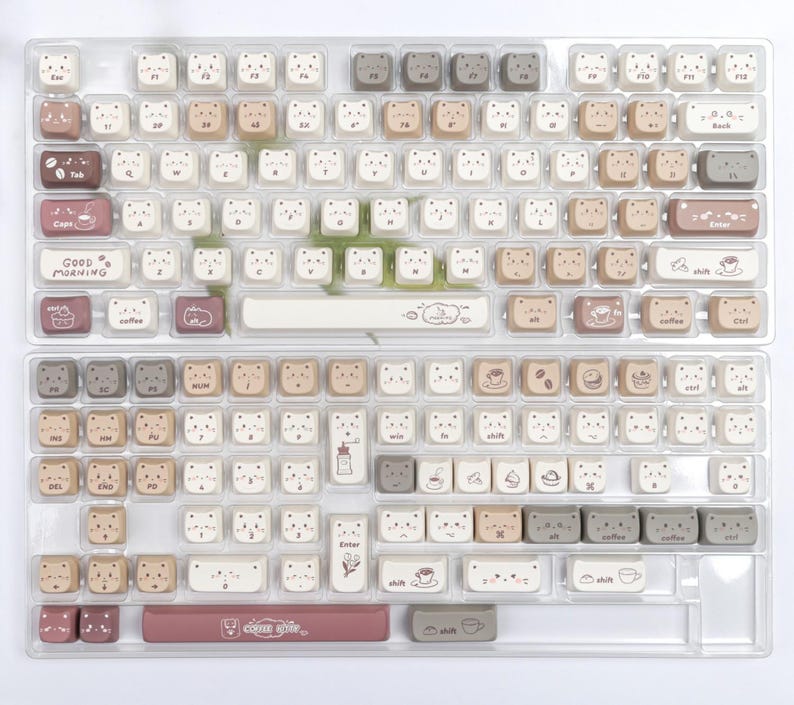 Puede incluir: Un conjunto de teclas de teclado en una bandeja de pl&aacute;stico transparente. Las teclas son principalmente blancas, beige y marrones, con dise&ntilde;os de caras de oso. Algunas teclas tienen gr&aacute;ficos tem&aacute;ticos de caf&eacute; y las palabras "Good Morning".