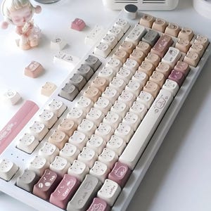 Puede incluir: Un teclado mec&aacute;nico blanco con teclas personalizadas en varios colores neutros, incluyendo blanco, beige y rosa. Las teclas presentan dise&ntilde;os de osos y caf&eacute;, con algunas teclas etiquetadas como "Tab", "Caps", "shift", "alt" y "coffee".