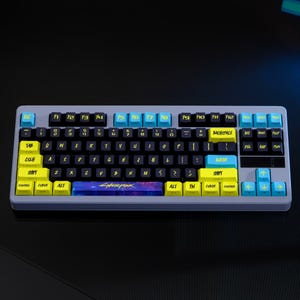 May include: A gray mechanical keyboard with black keys and yellow and blue accents. The keyboard has the word "Cyberpunk" on the spacebar. The keys are labeled with white letters and symbols.