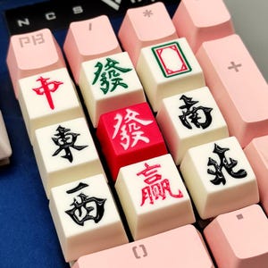 Puede incluir: Primer plano de un teclado mecánico con teclas personalizadas. Las teclas presentan diseños de fichas de Mahjong con caracteres chinos en rojo, verde y negro. Las teclas circundantes son de color rosa.