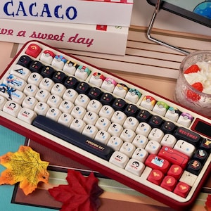 May include: A red and white mechanical keyboard with custom keycaps. The keycaps feature various designs, including Pokeballs and Japanese characters. The keyboard has a dark blue space bar with "POKEMON GO!" printed on it.