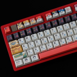 Pode incluir: Um teclado mecânico vermelho com teclas personalizadas com vários designs. As teclas têm imagens de Pokébolas, personagens e texto japonês. O teclado tem uma estrutura vermelha e um layout QWERTY padrão.