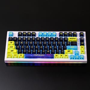 May include: A white mechanical keyboard with black, yellow, and blue keycaps. The keyboard features the word "CYBERPUNK" on the spacebar and has a rainbow LED light strip along the bottom edge. The keycaps have white lettering.