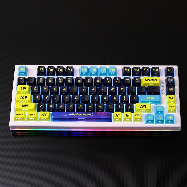 May include: A white mechanical keyboard with black, yellow, and blue keycaps. The keyboard features the word "CYBERPUNK" on the spacebar and has a rainbow LED light strip along the bottom edge. The keycaps have white lettering.