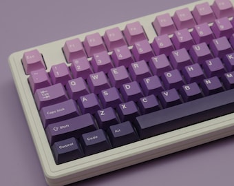 Puede incluir: Un teclado mecánico con un juego de teclas degradado púrpura. Las teclas cambian de rosa claro a púrpura oscuro. El teclado tiene un marco blanco y una barra espaciadora púrpura oscuro.