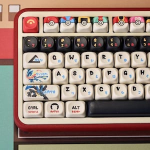 May include: A custom keyboard with a red frame and off-white keys. The keys feature various designs, including cartoon characters and Japanese characters. The top row has colorful ball-shaped keycaps. The keyboard has a black space bar and a red escape key.