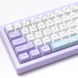 May include: A custom mechanical keyboard with a light purple frame and white keycaps. The keyboard features purple accent keys with cartoon character illustrations. The space bar is light blue with a cartoon character design.