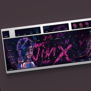 Op de afbeelding: Een witte mechanische toetsenbord met een levendig ontwerp, met het woord "JINX" in roze en paars. De toetsen zijn versierd met karakterkunst en pictogrammen. Het toetsenbord heeft een zilveren frame.
