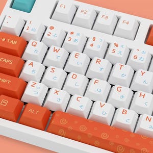 May include: Close-up of a white mechanical keyboard with orange and white keycaps. The keyboard has Japanese characters and English letters. The orange keys include the Tab, Caps Lock, Shift, Ctrl, and Alt keys.