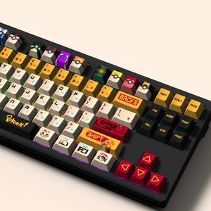 Puede incluir: Un teclado mec&aacute;nico negro con teclas personalizadas que representan personajes de Pok&eacute;mon. Las teclas son amarillas, rojas, azules, verdes y blancas con diferentes personajes de Pok&eacute;mon impresos en ellas. El teclado tiene un marco negro y un cable negro y blanco.