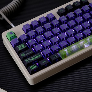 Pode incluir: Um teclado mecânico com teclas roxas e letras verdes. O teclado tem uma moldura bege e uma tecla Esc verde. As teclas estão dispostas em um layout QWERTY padrão, com caracteres japoneses em algumas teclas.