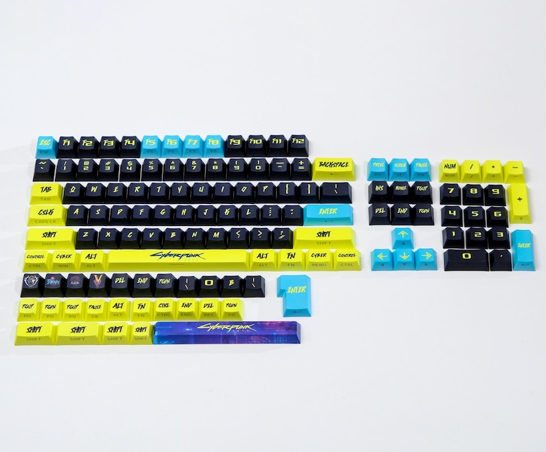 May include: A set of Cyberpunk-themed keyboard keycaps in various sizes and layouts. The keycaps are black, yellow, and blue, with the word "Cyberpunk" printed on the spacebar. The keycaps are designed for mechanical keyboards.