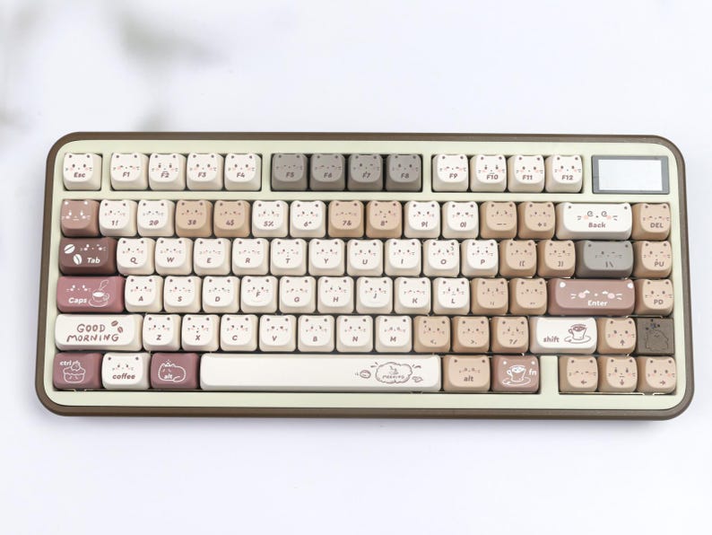 Puede incluir: Un teclado mec&aacute;nico beige y marr&oacute;n con teclas personalizadas. Las teclas presentan caras de oso e ilustraciones con tem&aacute;tica de caf&eacute;. El teclado tiene forma rectangular con esquinas redondeadas y el texto "Good Morning".
