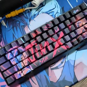 May include: A black mechanical keyboard with custom keycaps featuring a red and blue anime-style design. The keyboard is connected to a blue and white coiled cable. The keyboard rests on a matching mousepad.