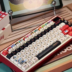 May include: A red and cream-colored mechanical keyboard with custom keycaps. The keycaps feature various designs, including Pokeball and character illustrations. The keyboard has a black space bar with "POKEMON GO!" printed on it.