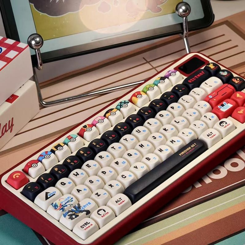 May include: A red and cream-colored mechanical keyboard with custom keycaps. The keycaps feature various designs, including Pokeball and character illustrations. The keyboard has a black space bar with "POKEMON GO!" printed on it.