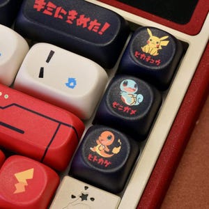 May include: Close-up of a custom keyboard with various keycaps. Some keycaps are navy blue with Pok&eacute;mon characters and Japanese text. Other keycaps are red, white, and beige. The keyboard has a red frame.