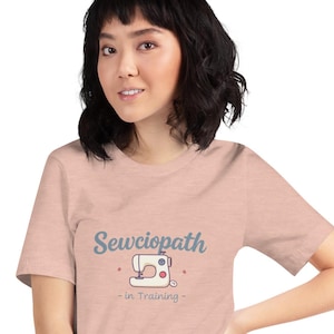 Peut inclure: Un t-shirt rose pâle avec un motif de machine à coudre bleu et blanc et le texte "Sewciopath - in Training -" imprimé sur le devant.