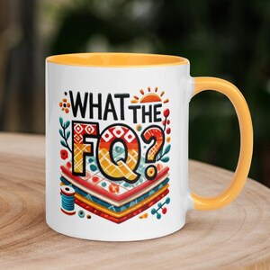 Könnte beinhalten: Weiße Keramiktasse mit gelbem Rand und Henkel. Die Tasse hat ein buntes Design mit dem aufgedruckten Text "What the FQ?"