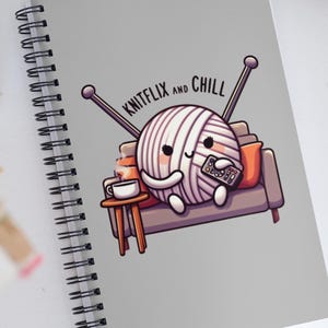 May include: A grey spiral notebook featuring a cute illustration of a ball of yarn relaxing on a sofa with a cup of coffee and a remote control. The text "Knitflix and Chill" is above the yarn ball.