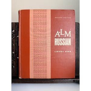 Puede incluir: Libro de texto A-LM Russian Level One, segunda edición, con una cubierta de color naranja rojizo. El título está en letras blancas. Una banda vertical de la palabra "Russian" en naranja claro recorre el lado izquierdo.