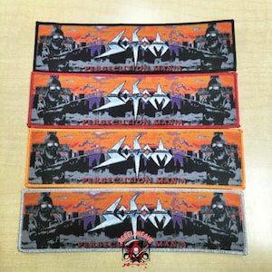 May include: Four rectangular embroidered patches featuring the Sodom logo and the text Persecution Mania. Each patch displays a graphic of a figure holding a rifle against an orange and purple background, with distinct black, red, orange, and grey borders.